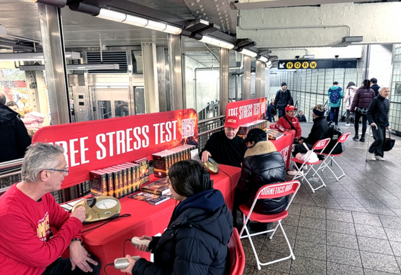 Dobrovolníci z Dianetiky nabízejí cestujícím na stanici metra Times Square 42nd Street v New Yorku bezplatné testy stresu během globální akce zaměřené na duševní zdraví, která zahrnovala 50 zemí a 250 měst (Hubbard Dianetics Foundation)