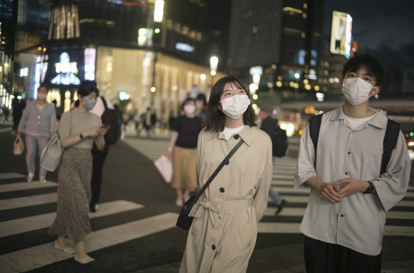 Muž a žena v maskách jdou přes křižovatku slavné nákupní čtvrti Ginza v Tokiu